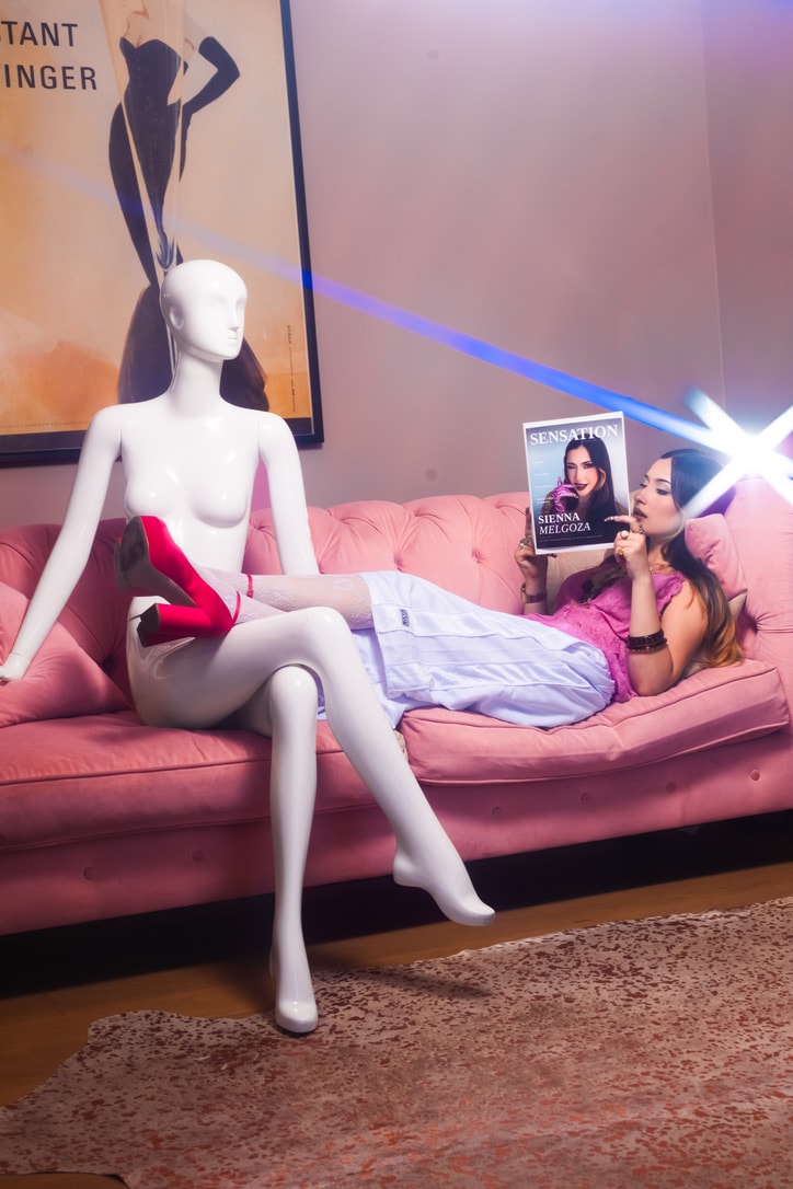 Sienna Melgoza reclining beside a mannequin on a pink sofa