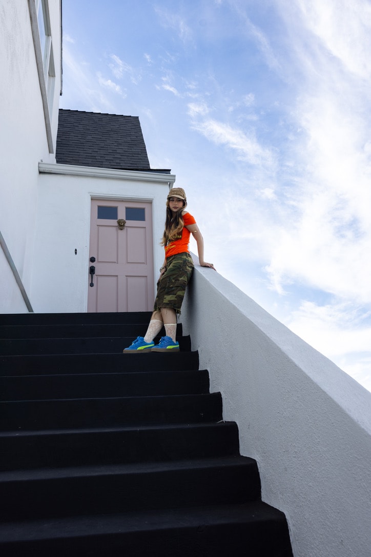 Sienna Melgoza standing on black stairs beside a white building